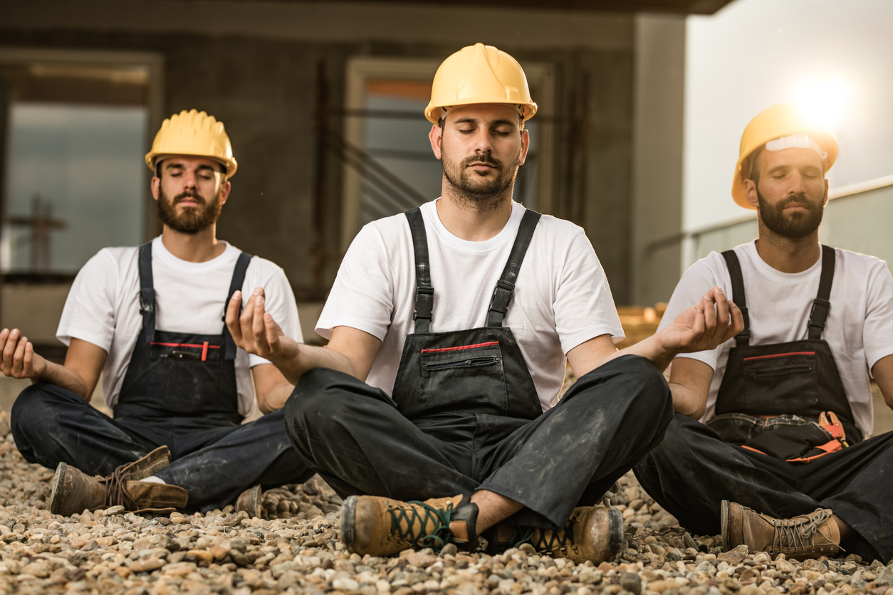 Team of manual workers meditating on a terrace of a construction site.