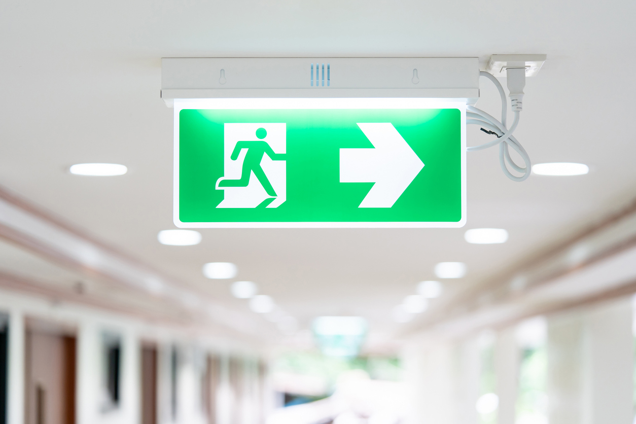 A Arrow light box sign of EMERGENCY FIRE EXIT is hung on the ceiling in hospital walkway, Idea for event fire or evacuation drills.