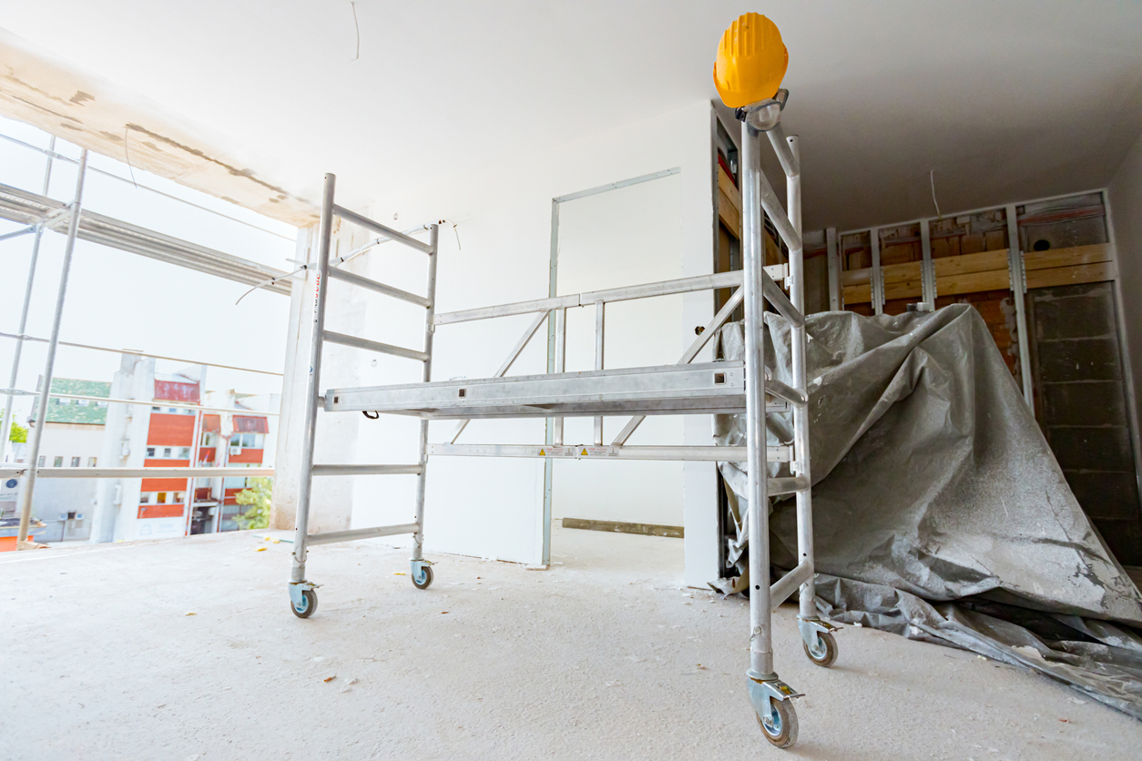 Moveable scaffold with wheels in the building under construction, yellow hardhat is on it