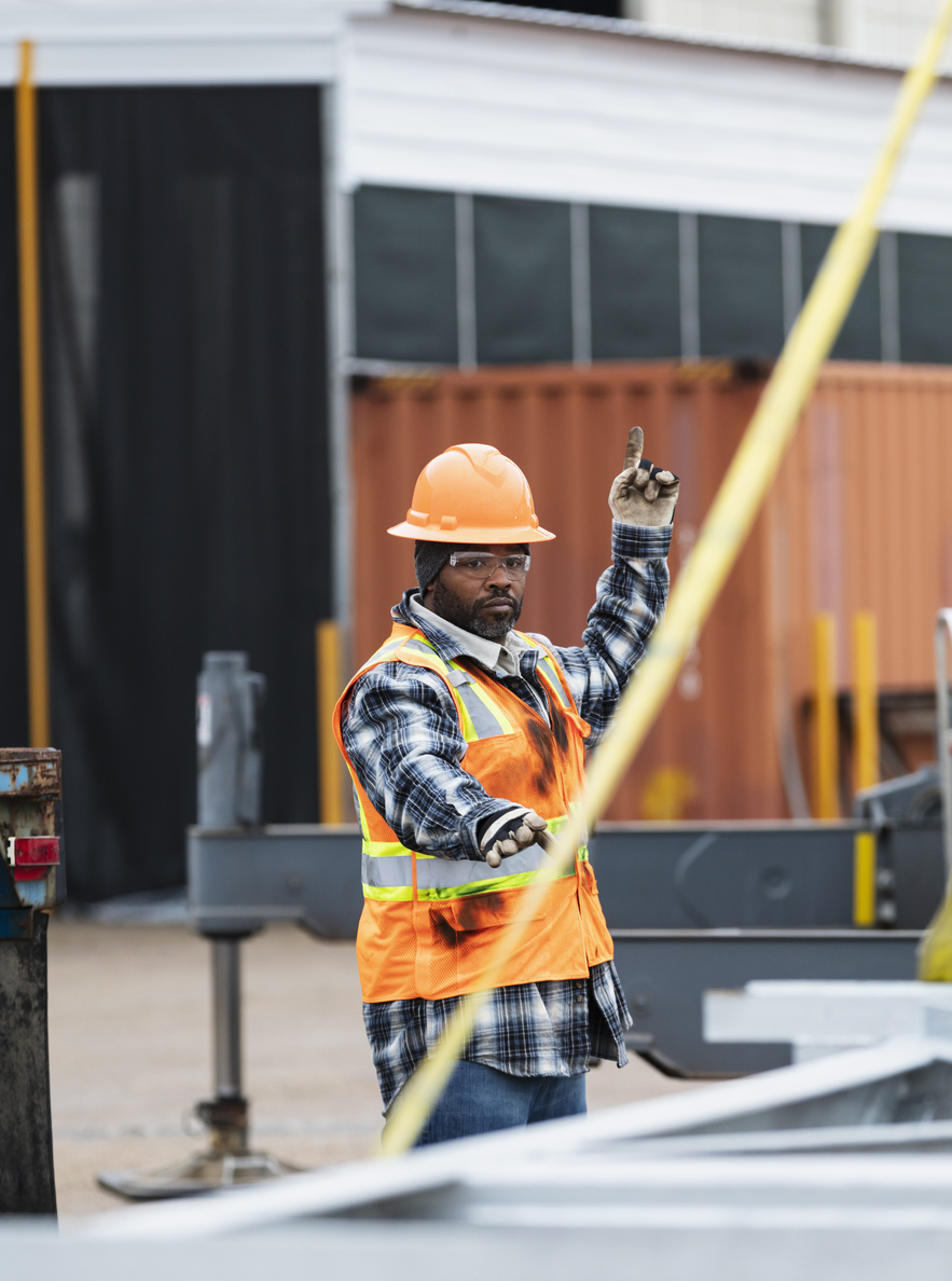 African American man assists crane operator lifting object