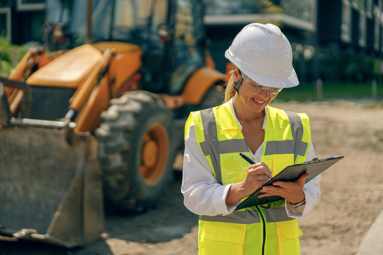 Professional female engineer in protective helmet making notes on construction site