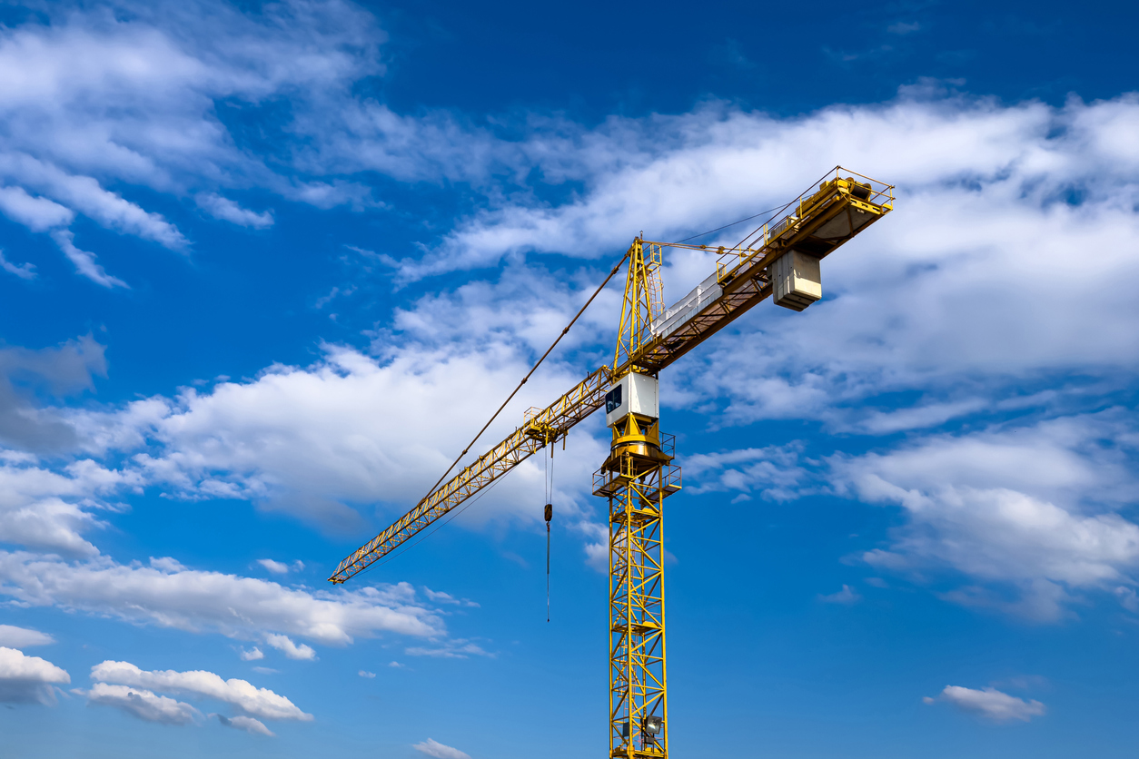 Yellow construction crane against a background of blue sky with light clouds.