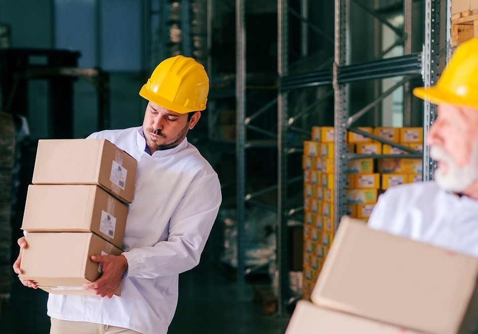 Two storage workers in work wear carrying heavy boxes.